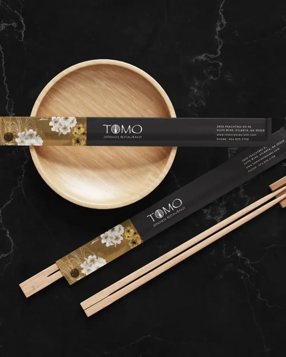 Tomo chopstick sleeves on black marble, carrying the sakura pattern and the logo
